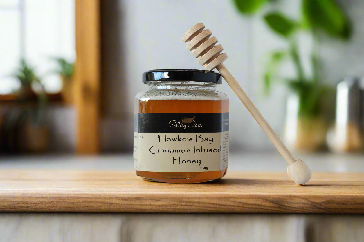 Jar of Hawke's Bay Cinnamon Infused Honey with a honey dipper on a wooden surface.